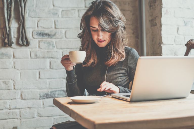 Woman drinking coffee and working on a laptop.