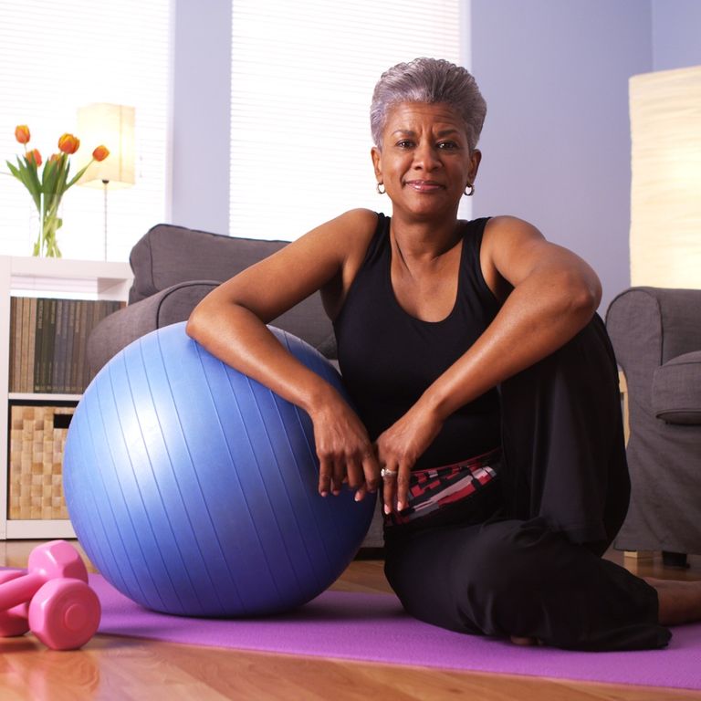 An older woman relaxing next to an exercise ball.